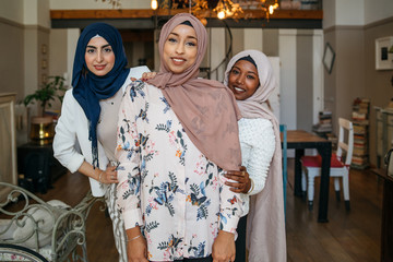 Portrait of three Muslim women with hijab at home - Arab millennials embrace in an apartment