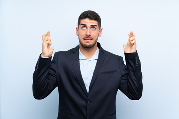 Handsome man over isolated blue background with fingers crossing and wishing the best