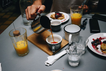 Delicious and healthy brunch or breakfast at fancy city hidden spot cafe, orange juice and wholewheat pancakes. Man pours organic filter specialty coffee from jar to cup. Food blogger