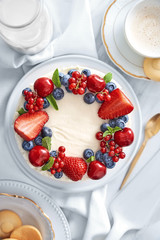 Fruit cake with berries coated in whipped cream on a light background viewed from above. Top view