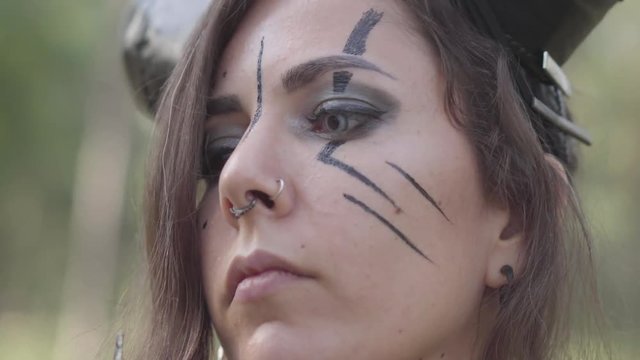 Close-up portrait of attractive forest fairy with big black horns on the head, eyes of different color and long claws on fingers dancing under the trees. The ancient ritual of forest creature