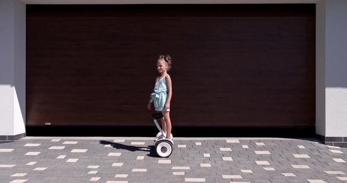 Little Girl rides a gyroscooter near the garage