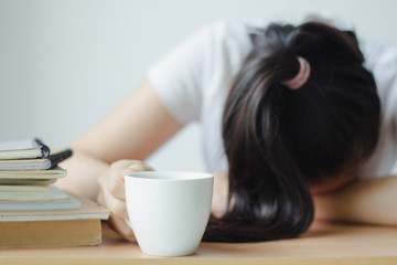 Tired young woman holding cup of coffee and lying sleeping on desk office with book and work.