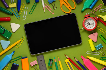 Modern digital tablet on a green background among office and school supplies. School office supplies on a desk with copy space. Back to school concept.