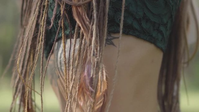 Close-up of dancing belly of attractive dryad or forest fairy with afro-braids and tattoo on the skin. The ancient ritual of forest creature. Performance of dancer in forest