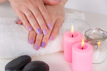 Obraz na płótnie Canvas Beautiful female hands with a lilac color manicure on a white towel and pink decoration candle burning on the desk in a beauty salon. Manicure and beauty concept. Close up, selective focus