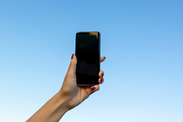 Woman hand with modern smartphone on on blue sky. Blank screen smartphone. Mobile communication network, information concept.