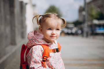 little pretty baby who got lost in the city, a girl in a pink raincoat, with a backpack and a...