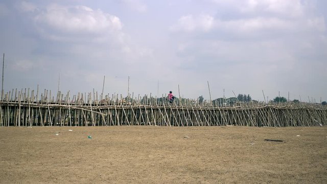 Projet motorbike crossing a bamboo bridge over a riverbed 