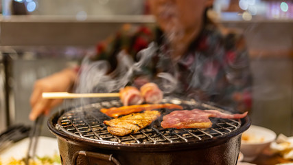 Grilling sliced pork and beef over stove in Japanese style with blurry woman in background