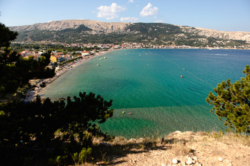 Adriatic Sea coastline in Croatia. Rocky shore with turquoise water. Baska island, touristic destination in Croatia. Panoramic scene of Baska Beach. Mountains in the background. First plan in defocus.