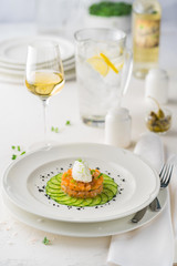 The salmon Tartar with cheese souffle on a white plate surrounded by Cutlery and white wine