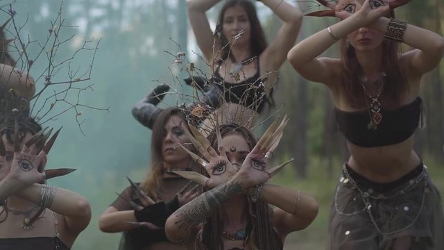 Dryads or forest fairies with painted eyes on the palms and false claws moving fingers with long claws in the cloud of the smoke. Performance of dancers in forest. Slow motion.