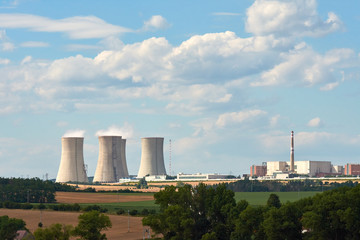 View of smoking chimneys of nuclear power plant, power lines and forest, under blue sky with clouds