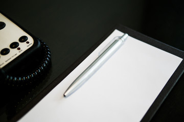 the silver pen color is placed on white short note paper on the brown wooden table near telephone...