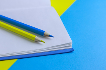 Yellow and blue pencils and notebook on color background 