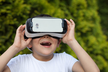 Cute little boy using VR glasses outdoors in a park - Blogger testing augmented reality goggles...