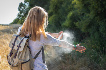 Woman tourist applying mosquito repellent on hand during hike in nature. Insect repellent. Skin protection against tick and other insect. - obrazy, fototapety, plakaty