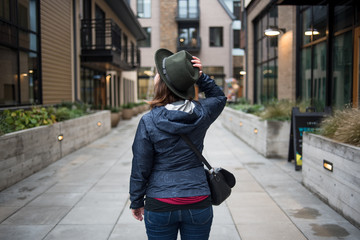 Woman from behind in residential alley holding hat on head with hand