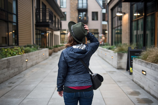 Woman from behind in residential alley holding hat on head with hand