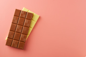White and black chocolate bars over pink background, copy space.