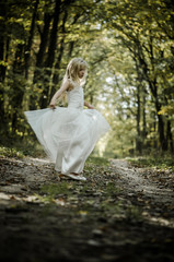 adorable blond girl dancing in sunny day in magical forest