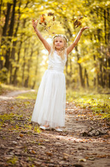 adorable blond girl with leaves in hands in sunny day in magical forest