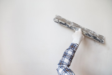 Worker in white gloves performs plastering of the walls of the room.