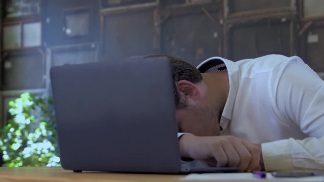 Tired businessman sleeping on a laptop in small business office for startup team.