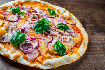 Pizza with Mozzarella cheese, ham, tomato sauce, onion, pepper, Spices and Fresh basil. Italian pizza on wooden table background