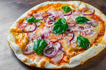 Pizza with Mozzarella cheese, ham, tomato sauce, onion, pepper, Spices and Fresh basil. Italian pizza on wooden table background