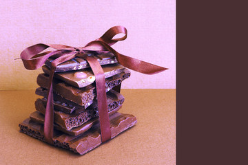 A stack of broken chocolate of different varieties tied with a brown satin ribbon on a brown background. Layout for design. Space for text...