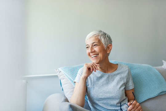 Happy woman relaxing on her couch at home in the sitting room. Portrait of beautiful mature woman smiling while sitting at sofa at home. Beautiful middle age woman smiling at home