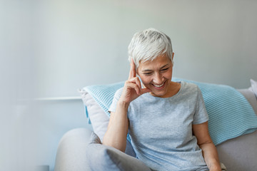 Happy mature woman relaxing by the window. The joys of retirement Smiling mature woman sitting by window at home. Portrait of beautiful mature woman.