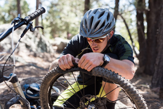 Man fixing flat mountain bike tire on trail