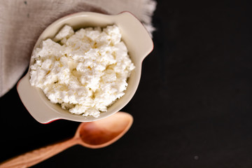 dairy product cottage cheese in brown ceramic bowl with spoon on vintage wooden table