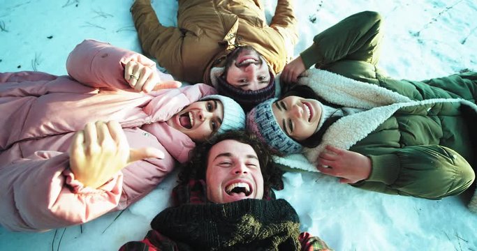 Group of multi ethnic friends enjoying the time together in a winter time they laying down on the floor make a circle and make a funny faces and enjoying the time