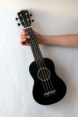 Obraz na płótnie Canvas Ukulele, a small black guitar, in the girl's hand on a white background