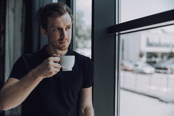 Handsome man with cup standing near the window