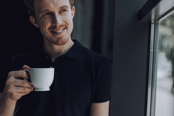 Attractive man with coffee by the window looking glad