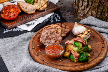 Fried meat medallions with braised Brussels sprouts, grilled garlic and barbecue sauce on round wooden board