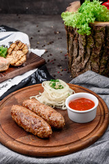 Fried meat sausages, served with pickled onions and barbecue sauce on a round wooden board on dark concrete background