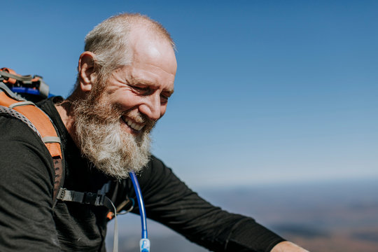 Retirement age hiker with a beard smiles at the top of Mount Katahdin