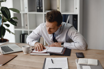 Obraz premium Attentive businessman leaning tot eh table and looking at plans