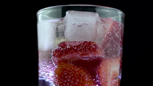 Tall glass soda water with ice cubes and strawberries, centre screen. Fizzy bubbles rising. Rotating in slow motion.