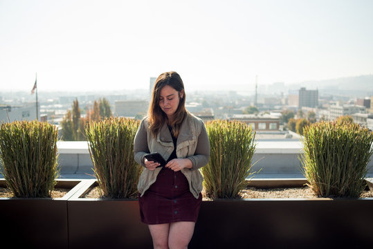 Photo of woman checking smartphone on rooftop with view behind her