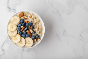 Oatmeal porridge with blueberries, almonds and banana on marble table