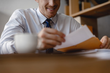 Smiling young man opening the envelope at work