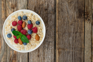 Oatmeal with raspberries, almonds and blueberries and mint on old wood background