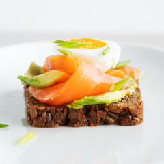 Healthy open sandwiches on multigrain wholegrain  toast with avocado, salmon, eggs, herbs, sunflower seeds over white plate on concrete background with copy space. Healthy protein food.